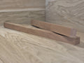 To lange, smalle træstænger i kirsebærtræ med glat, naturlig finish, placeret diagonalt på lyst træbord.