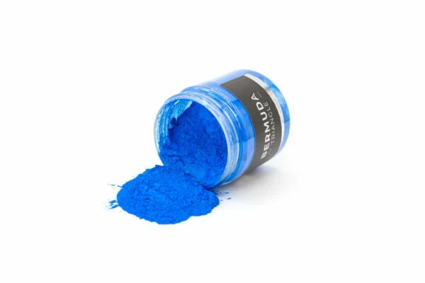 Låg åben krukke med skinnende, himmelblåt metallic pigment spildt på hvidt underlag.