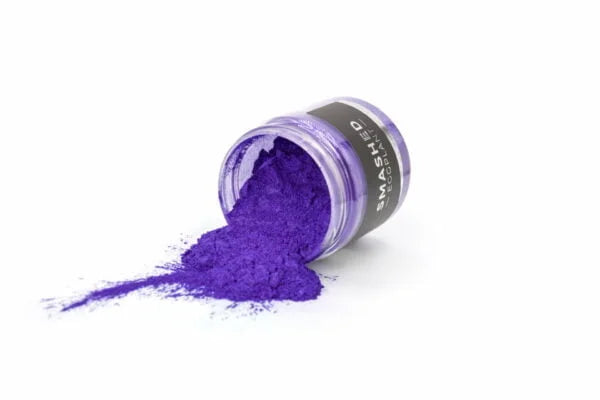 Lille glas med violet metallic mica pigment spildt ud på hvid baggrund.